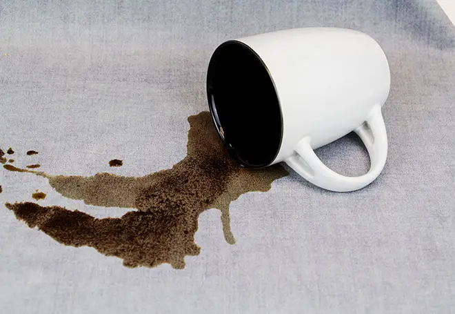 Pessoa removendo café derramado em camisa branca com guardanapo para ensinar como tirar mancha de cafe do tecido.